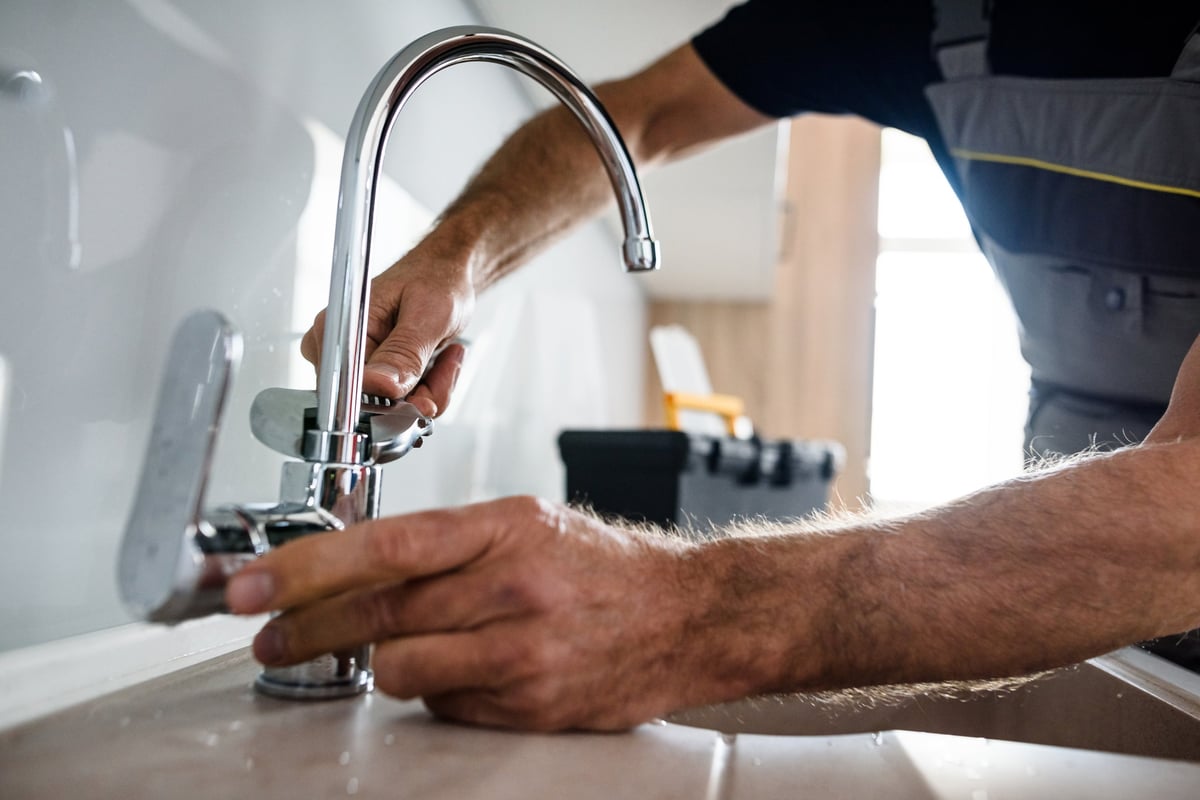 Close up of hands of aged repairman in uniform working, fixing broken kitchen tap using adjustable wrench